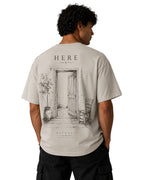 ArvoCulture oversize tişört, arkasında HERE yazısı ve kapı, sandalye, saksıda ağaç çizimi. Açık gri pamuklu kumaş.
